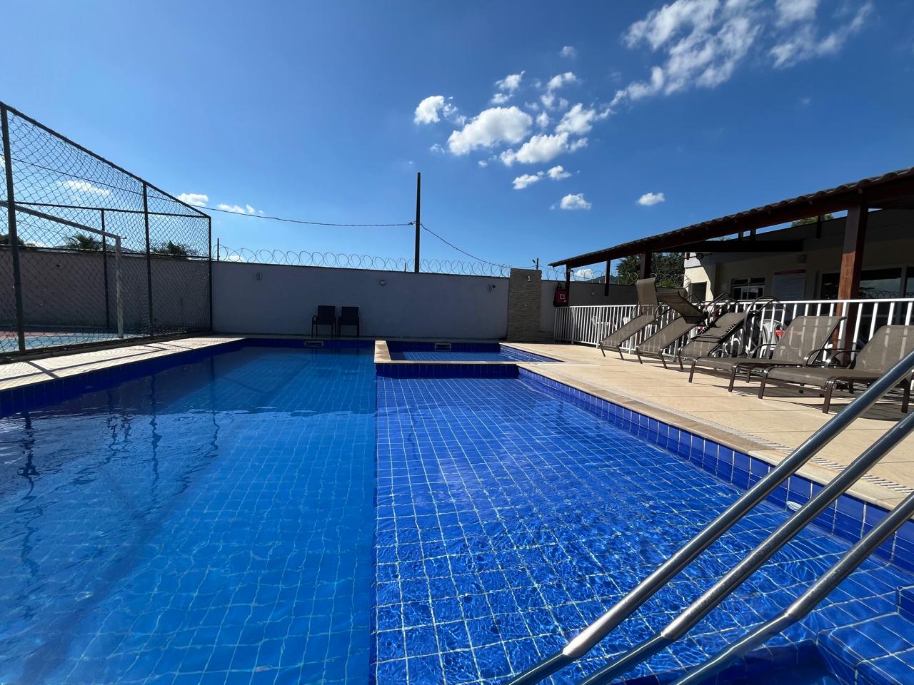 Piscina do condomínio com área de descanso e paisagismo